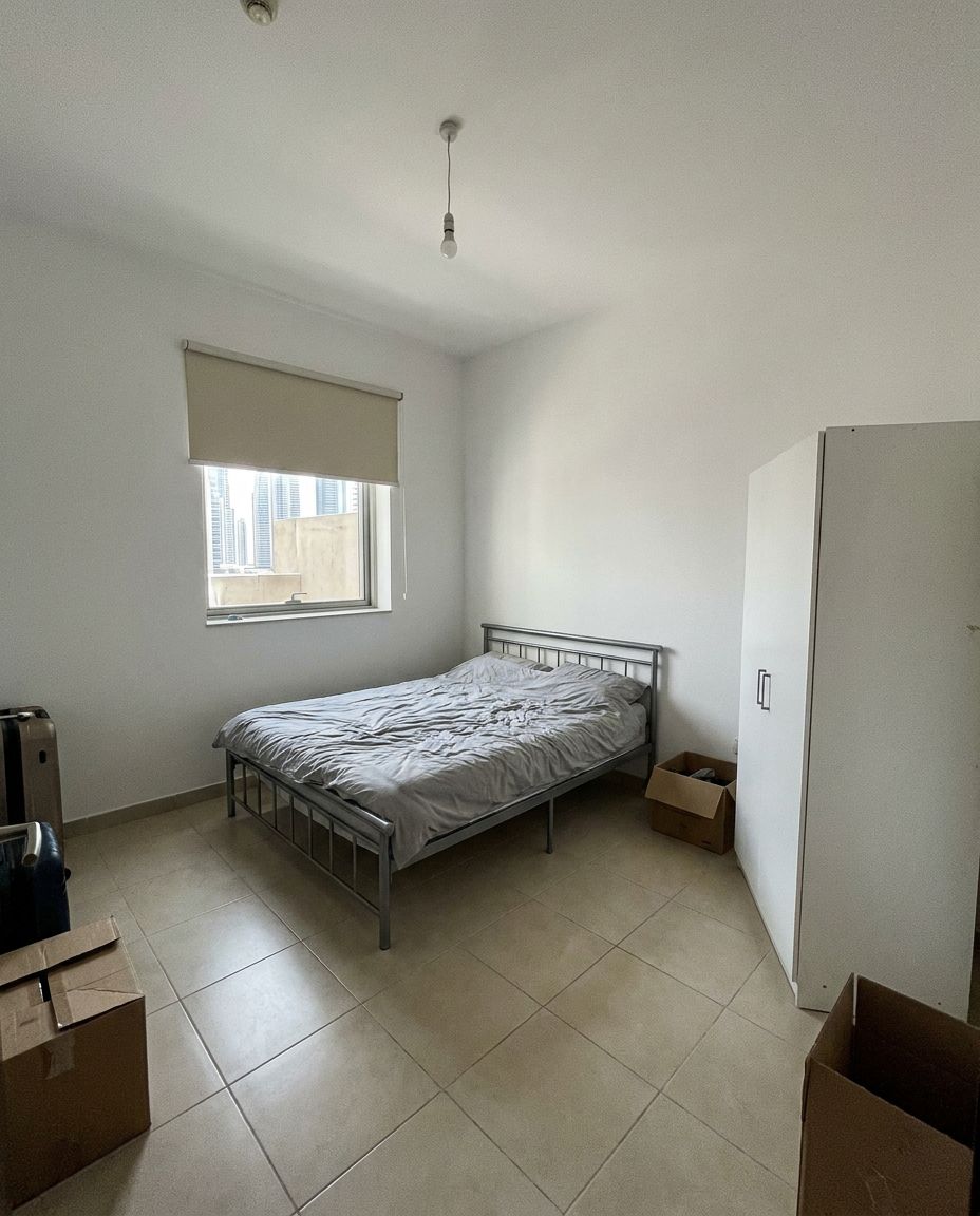 Abu Dhabi apartment bedroom before: metal bed, bare walls and moving boxes